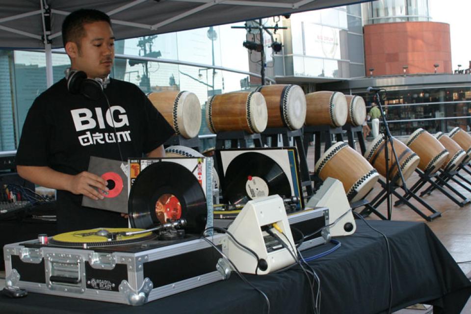 Masaki Miyagawa stands behind a turntable pulling a record to spin before the Kinnara Taiko performance begins